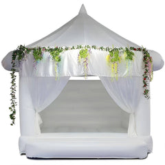 White commercial-grade wedding bouncy house by Soft Summits with decorative plants for outdoor wedding celebrations.